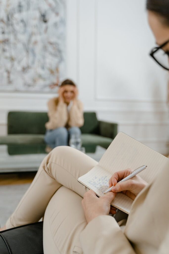 A therapist takes notes in a modern office setting during a therapy session with a patient.